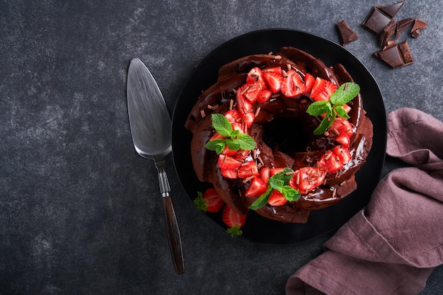 Dark Chocolate Bundt Cake with Ganache Icing and strawberry on dark stone or concrete table background Festive cake Selective focus