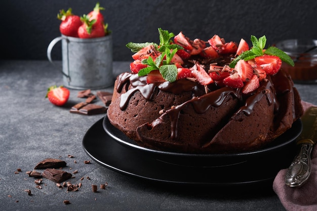 Dark Chocolate Bundt Cake with Ganache Icing and strawberry on dark stone or concrete table background Festive cake Selective focus