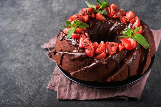 Dark Chocolate Bundt Cake with Ganache Icing and strawberry on dark stone or concrete table background Festive cake Selective focus