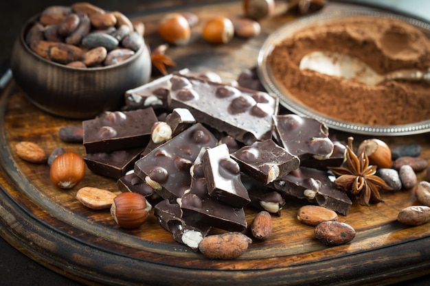 Dark chocolate in a composition with cocoa beans and nuts, on an old background.