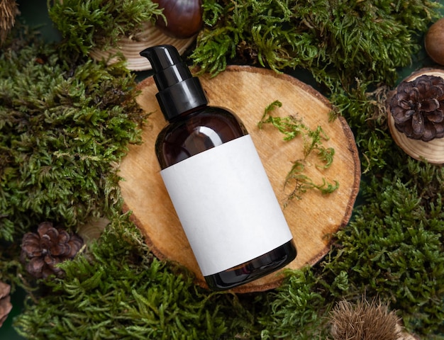 Dark Cosmetic bottle with blank label on wooden piece between green moss top view mockup