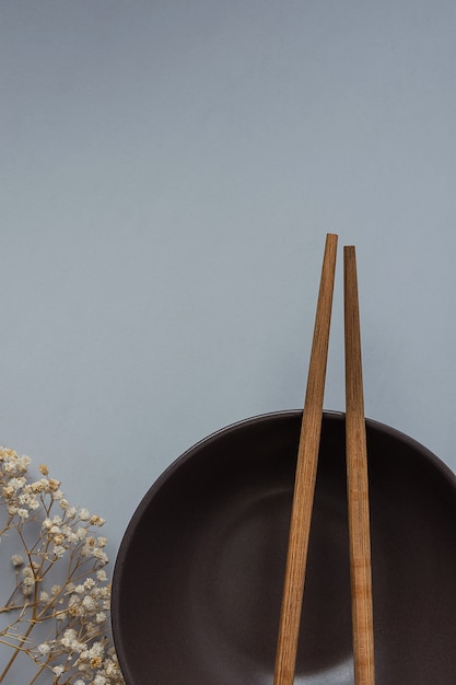 Dark Empty Bowl with Brown Chopsticks on Grey Background Twig of Dry Small White Flowers.