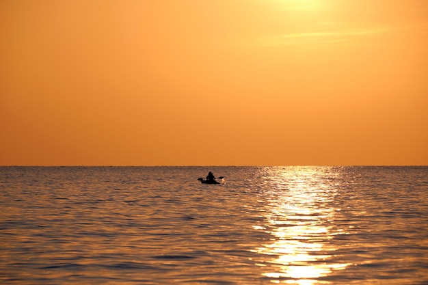 Dark figure of sportsman rowing alone on his kayak boat on sea water at sunset Active extreme sports concept