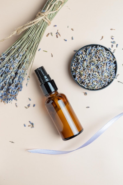 Dark glass bottle with cream or fluid of lavandula scattered flowers of dried purple lavender blossom on on beige background Herbal aromatherapy and skincare