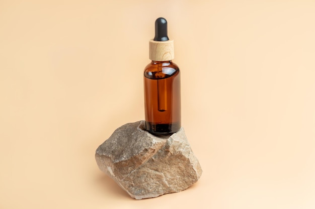 Dark glass cosmetic bottle with a dropper on a beige background with stone and copy space Natural cosmetics concept natural essential oil and skin care products Mockup