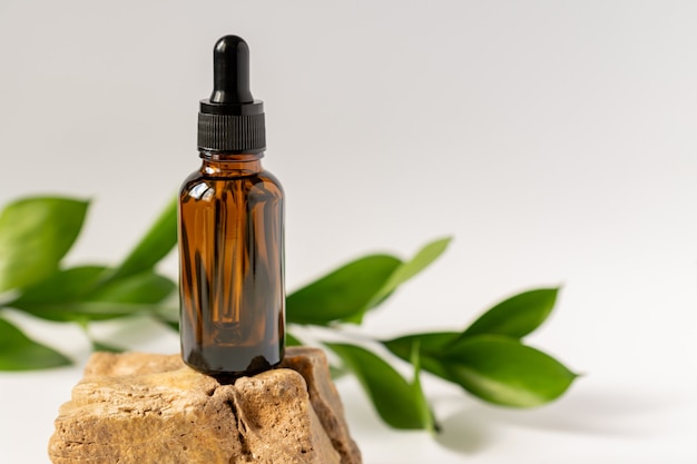 Dark glass cosmetic bottle with a dropper on a grey surface with stones and tropical leaves