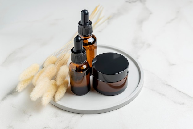 Dark glass cream jar and dropper bottles with face oil on a ceramic tray Cosmetic container mockups Background for branding and packaging presentation Natural skincare beauty product concept