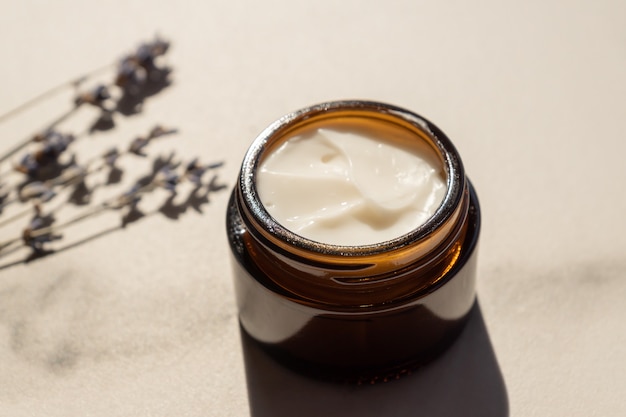 Dark glass jar with cream of lavandula, flowers of dried purple lavender blossom on marble table. Herbal aromatherapy and skincare.