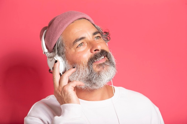 Dark gray haired middle aged man 40s 50s in casual sweater listening to music with headphones isolated on pink background studio portrait