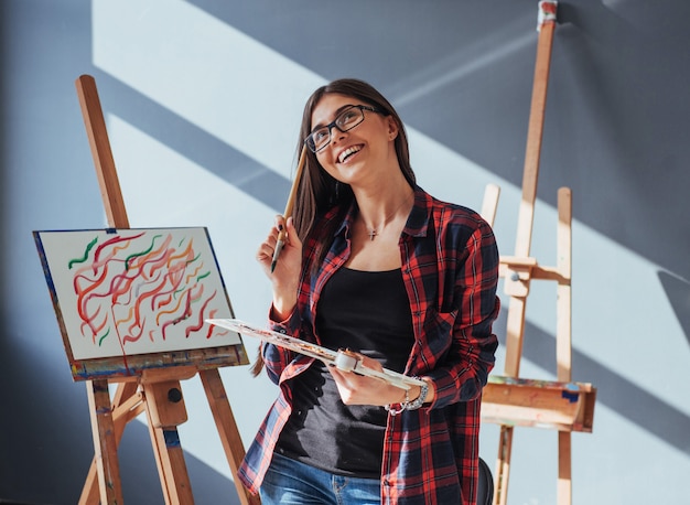 Dark-haired artist holding a brush in his hand and draws a picture on canvas.