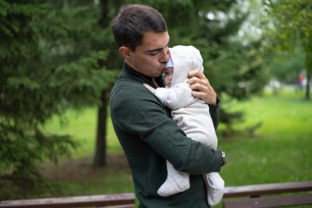 Dark haired dad in green jacket kisses his infant baby in hands happy fatherhood unconditional love