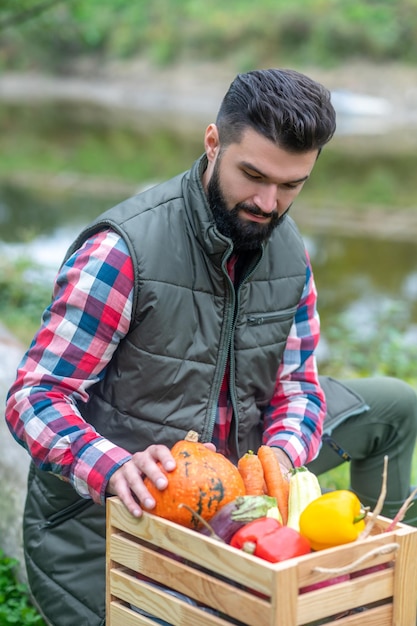 A dark-haired man in plaid shirt with a box with veggies