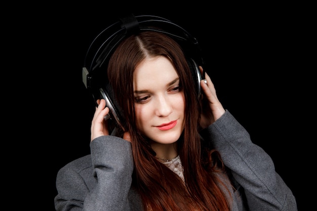 Dark haired model is posing in a dark studio with a headphones on her head