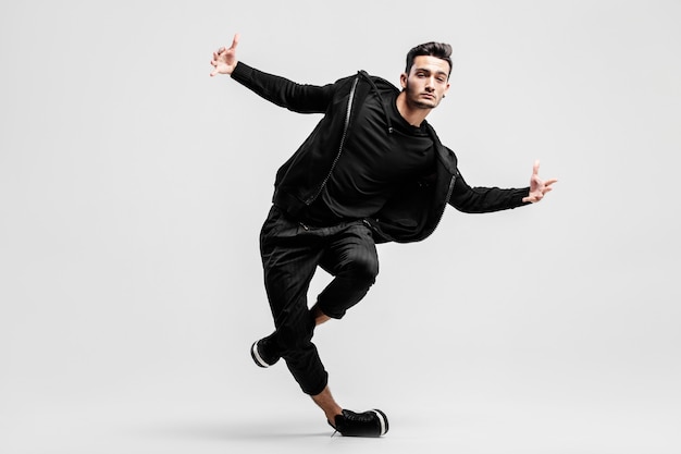 Photo dark-haired stylish young man wearing a black sweatshirt and black pants makes stylized movements of street dances