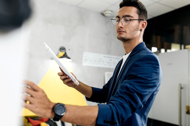 Dark-haired young architect dressed in blue checkered jacket works in the modern office .