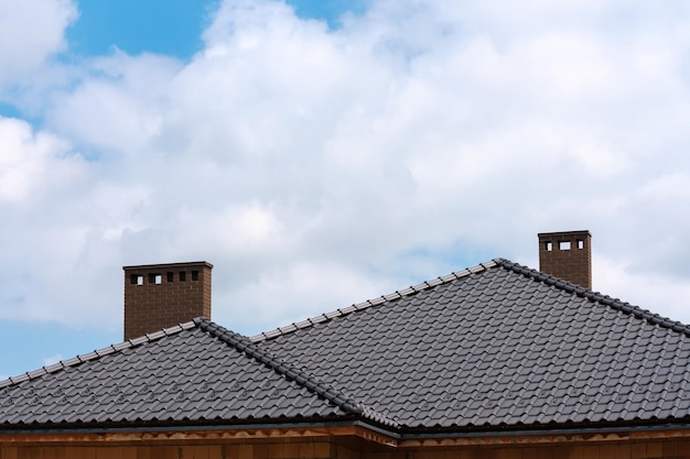 Dark metal tile shingles roof with chimney against blue sky with white clouds