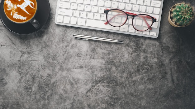 Dark office desk workplace with keyboard computer eyeglass pen and cup of coffee Top view flat lay with copy space