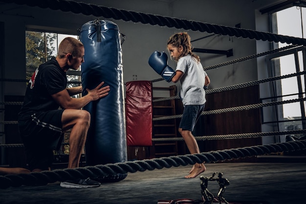 Dark photo shoot of kids training with big punching bag at boxing studio.