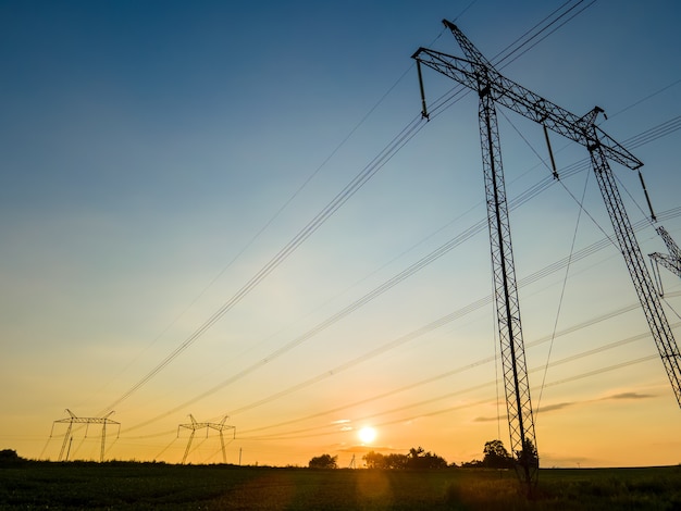 Dark silhouette of high voltage towers with electric power lines at sunrise.