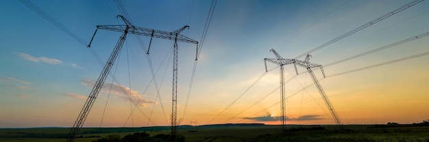 Dark silhouette of high voltage towers with electric power lines at sunrise.