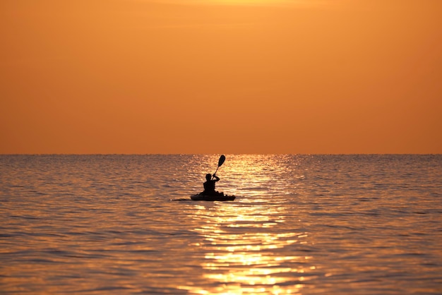 Dark silhouette of lonely fisherman rowing on his boat on sea water at sunset