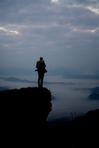 Dark silhouette of man photographer on the cliff and beauty mist at morning.