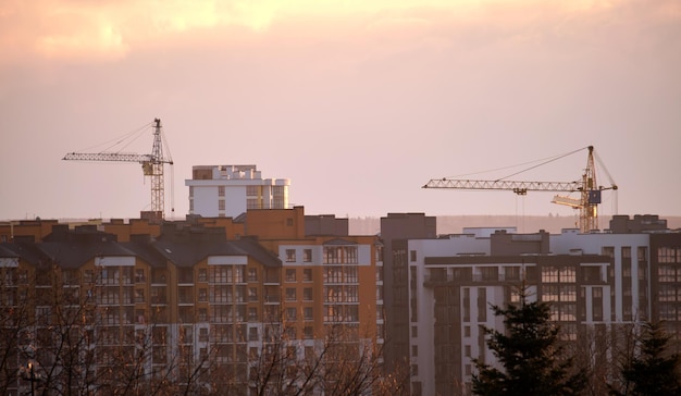 Dark silhouette of tower cranes at high residential apartment buildings construction site at sunset Real estate development