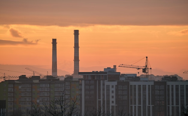 Dark silhouette of tower cranes at high residential apartment buildings construction site at sunset Real estate development