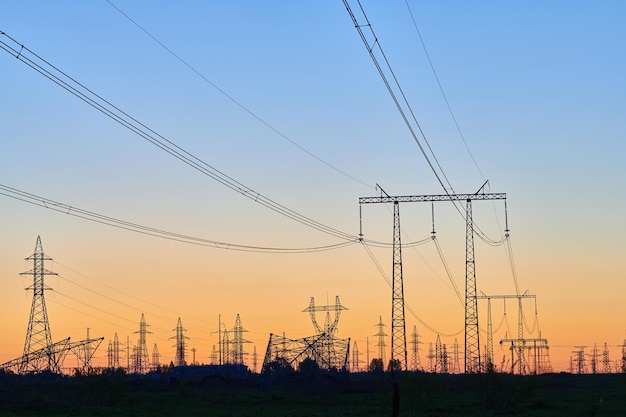 Dark silhouettes of power lines on fiery sunrise High voltage electricity towers in field and fiery sunset Concept of crisis of energy consumption generation and supply