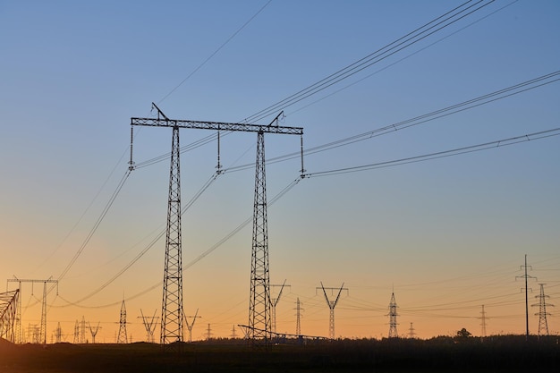 Dark silhouettes of power lines on fiery sunrise High voltage electricity towers in field and fiery sunset Concept of crisis of energy consumption generation and supply