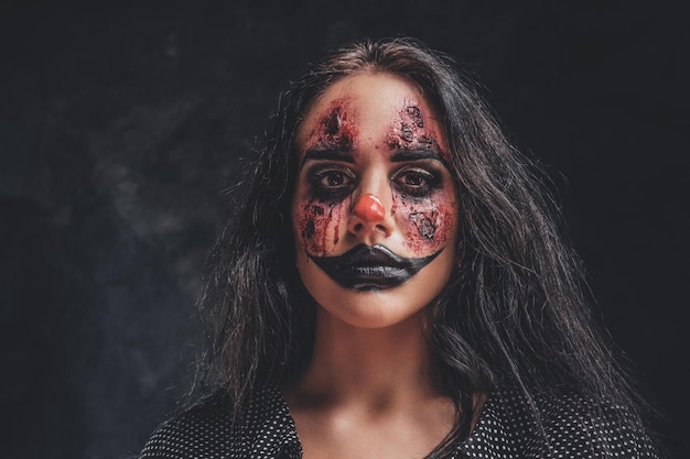 In the dark, smoky photo studio young girl has a photo shoot in a role of creepy clown.