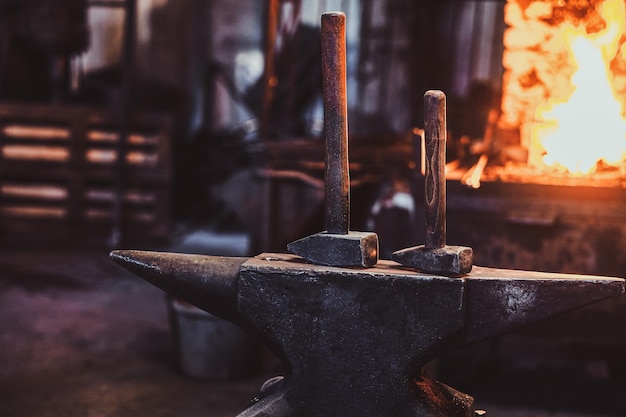 Dark stithy workshop with hammer on anvil at firs plan and fire in stove at background.