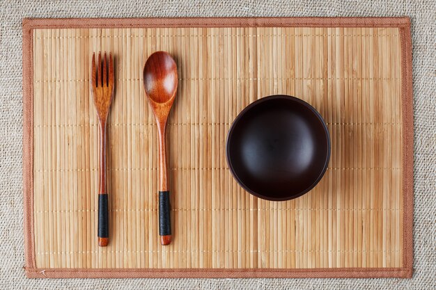 Dark wood spoon, fork and empty cup on bamboo backing in Asia.