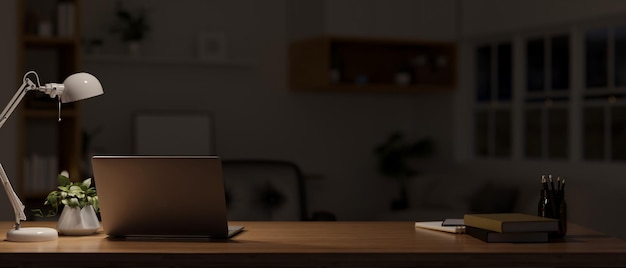 Dark workspace at night with laptop stationery table lamp and decor on wood tabletop