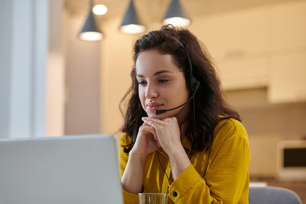 Darkhaired woman in a mustard shirt at her working place