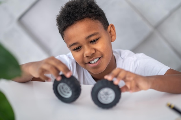 A darkskinned boy playing with toy vehicle wheels