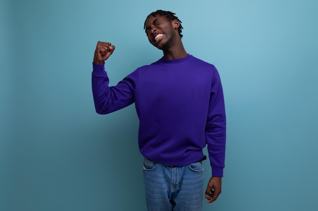 Darkskinned young brunette man with dreadlocks in a blue sweatshirt shows muscles