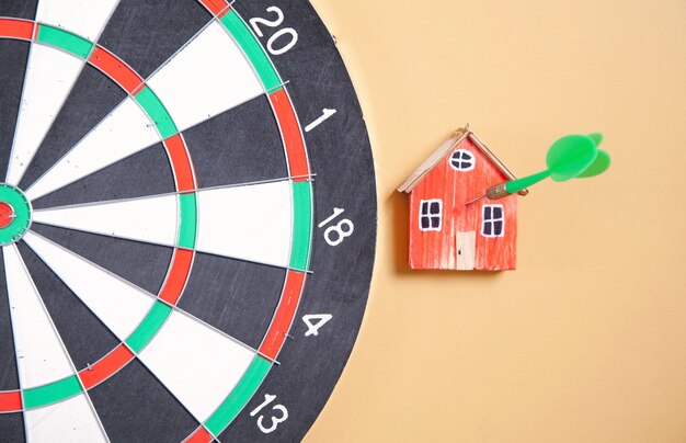 Dart arrow, dartboard and house model on yellow background.