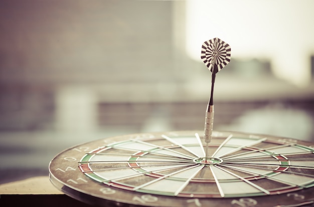 Dart arrow hitting in the target center of dartboard with modern city and sunset background. 