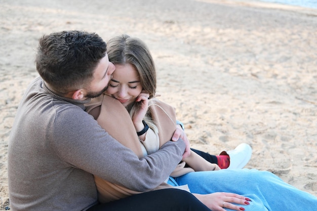 Date on the beach in the cold season The guy hugs the girl from behind by the shoulders and kisses her on the forehead