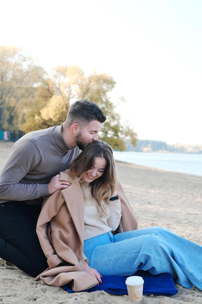 Date on the beach in the cold season The guy hugs the girl from behind by the shoulders and kisses her