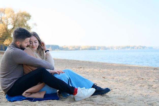 Date on the beach in the cold season The guy hugs the girl from behind by the shoulders and tries to warm her