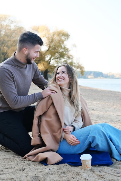 Date on the beach in the cold season The guy puts a coat on the girl's shoulders