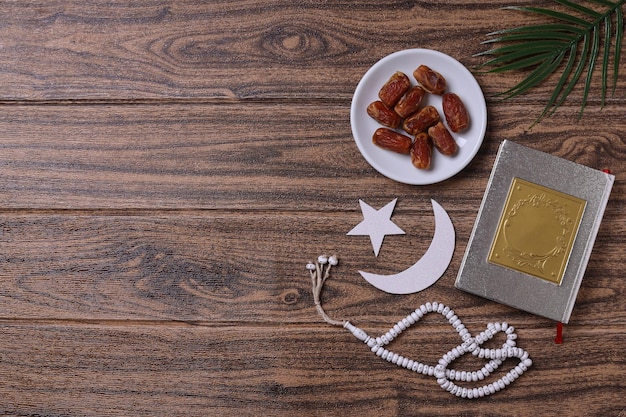 Dates fruit with koran, prayer beads and islamic decoration on wooden background