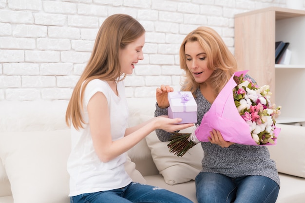 The daughter gives her mother flowers and gifts.