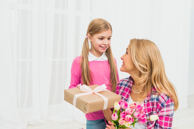 Photo daughter giving gift to mother with flowers