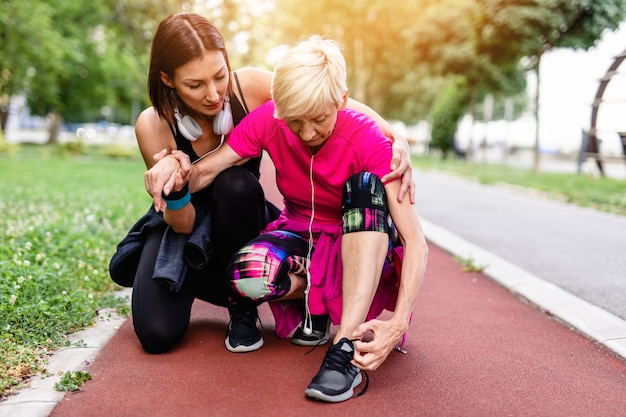 Daughter helping her mother who has pain in ankle after jogging.