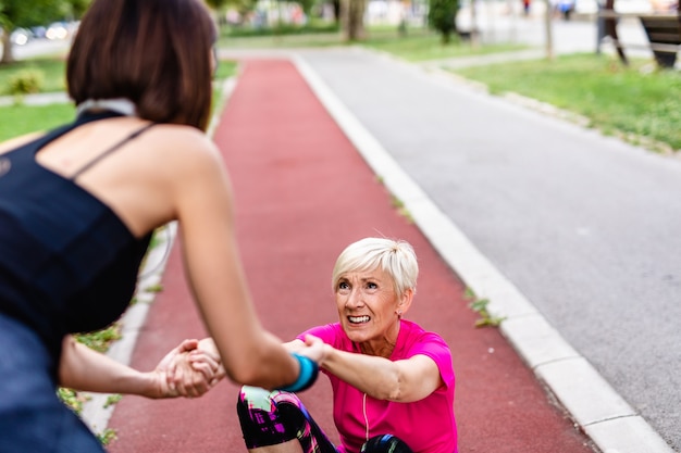 Daughter helping her mother who has pain in ankle after jogging.