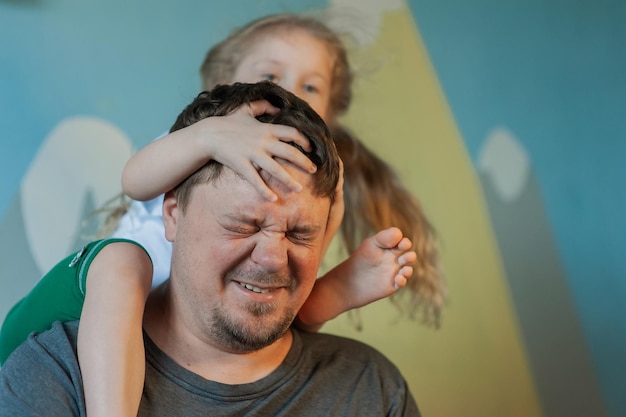 Daughter plays with dad crawling over him climbing onto his neck at home