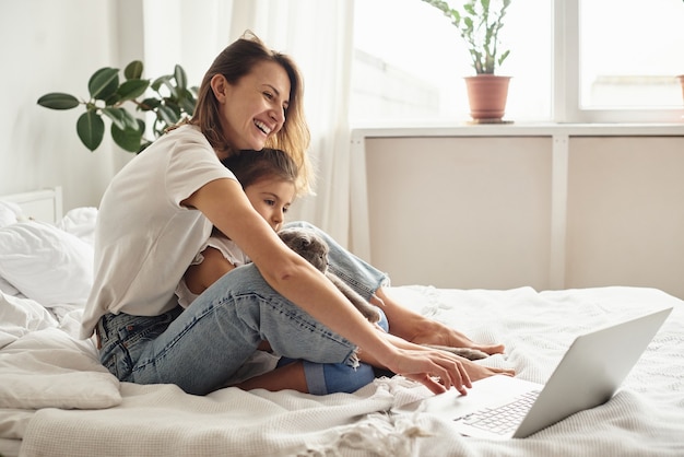 Daughter plays with mom and cat while mom works on computer